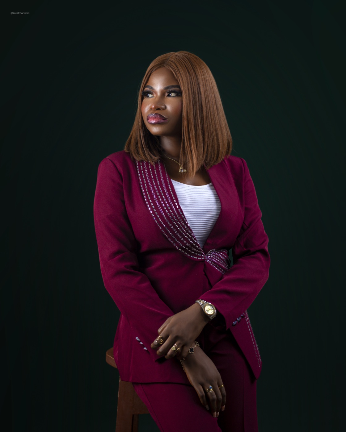Damola Kenny in a burgundy suit, seated studio portrait